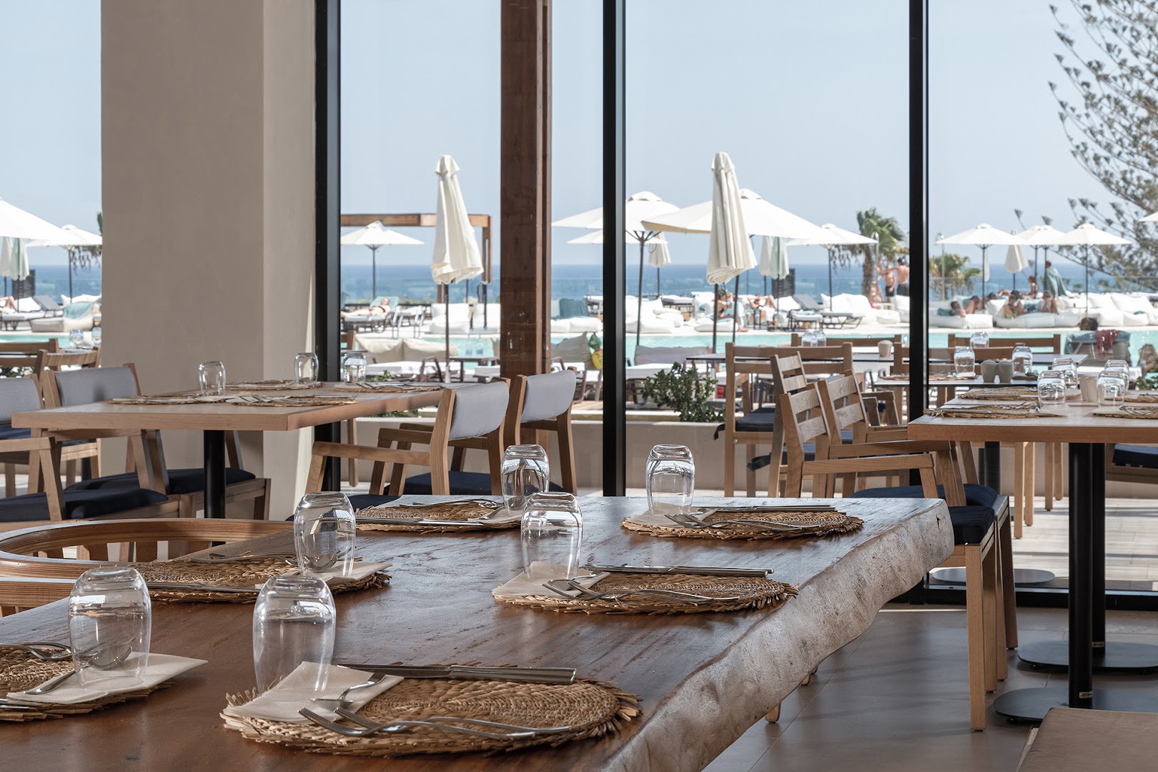 Helea Lifestyle Beach Resort restorāns ar panorāmas logiem, koka galdiem un skatu uz baseinu un jūru