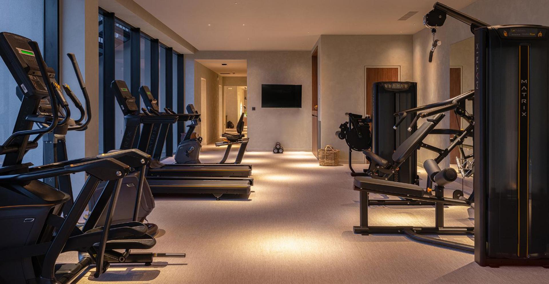 Helea Lifestyle Beach Resort modernā fitnesa zāle ar Matrix trenažieriem, skrejceļiem un plašiem logiem Rodas salā, Grieķijā
