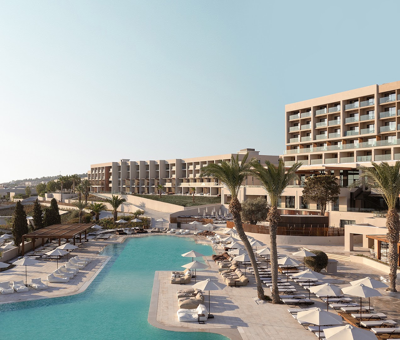 Helea Lifestyle Beach Resort modernā arhitektūra ar lielu āra baseinu, atpūtas krēsliem, saulessargiem un palmām saulainā dienā Rodā