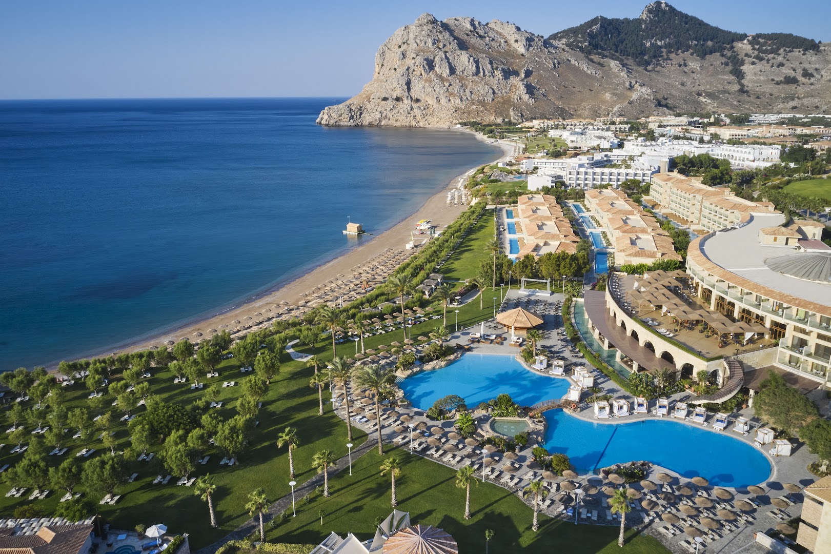 Atlantica Imperial Resort plašā teritorija ar lielu baseinu ar pārplūdes malu, atpūtas krēsliem un skatu uz jūru un kalniem