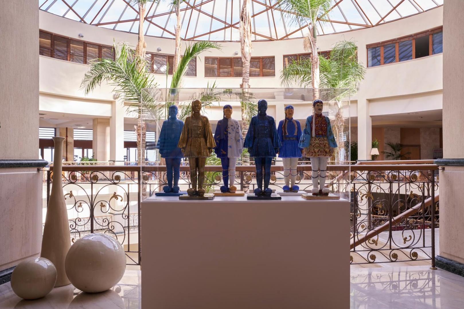 Atlantica Imperial Resort viesnīcas vestibils Rodā ar mākslas ekspozīciju stikla vitrīnā, palmām un plašu stiklotu jumta konstrukciju