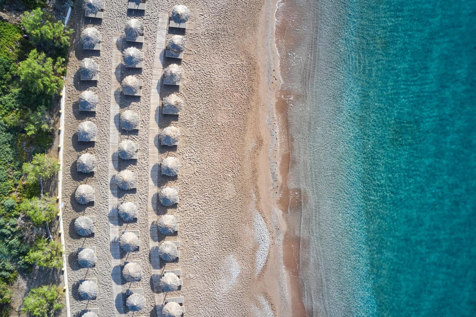 Atlantica Imperial Resort privātā pludmale no putna lidojuma — sakoptas saulessargu rindas, smiltis un dzidrs tirkīza krāsas ūdens Rodā