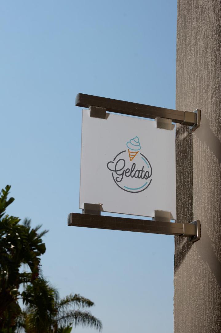 Atlantica Aegean Blue viesnīcas gelato saldējuma kafejnīcas izkārtne pie ēkas sienas uz zilu debesu un palmu fona