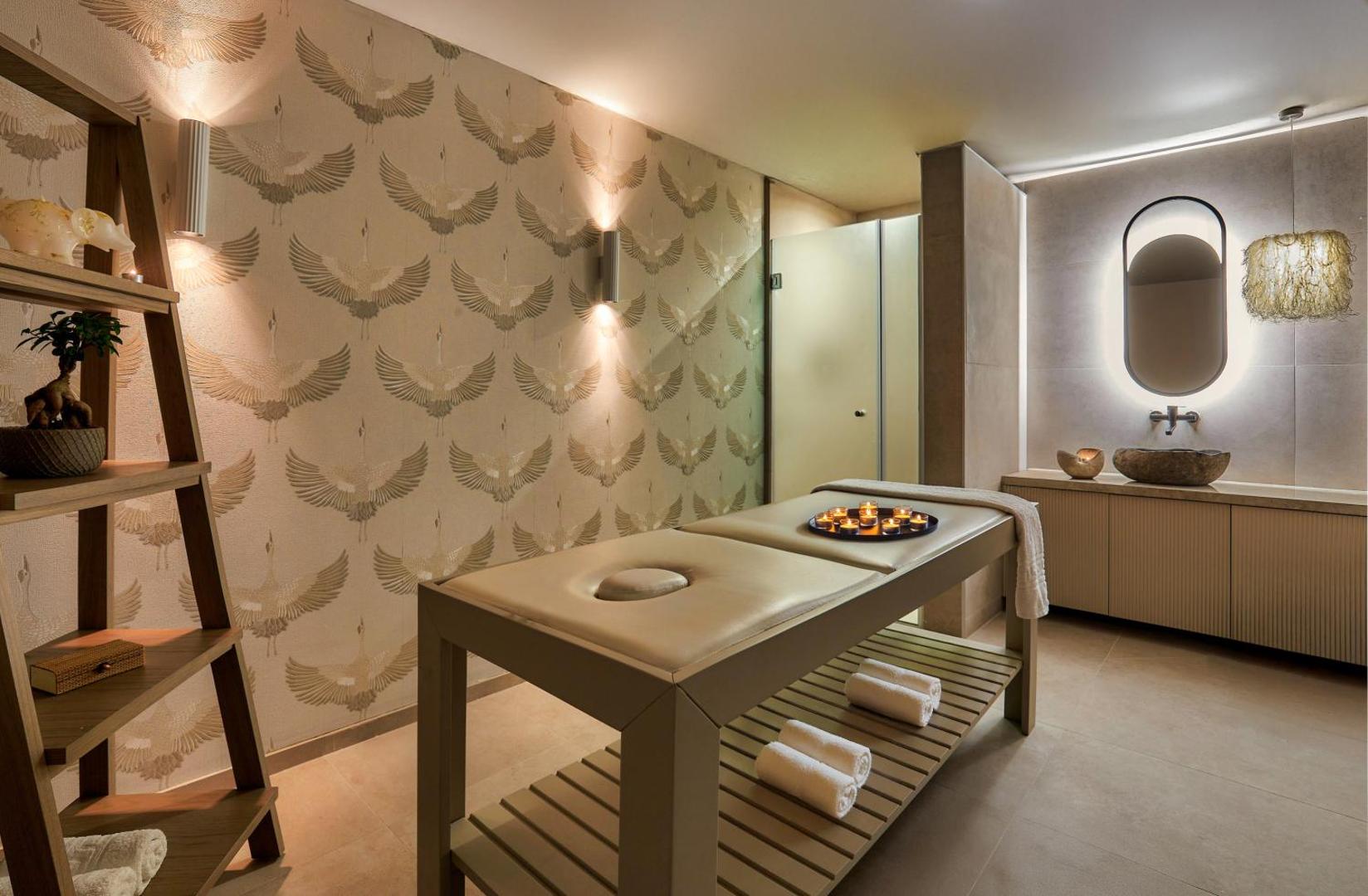 Blue Marine Resort & Spa masāžas telpa ar modernu dizainu, divvietīgu masāžas galdu, svecēm un stilīgu sienas dekoru ar dzērvēm.