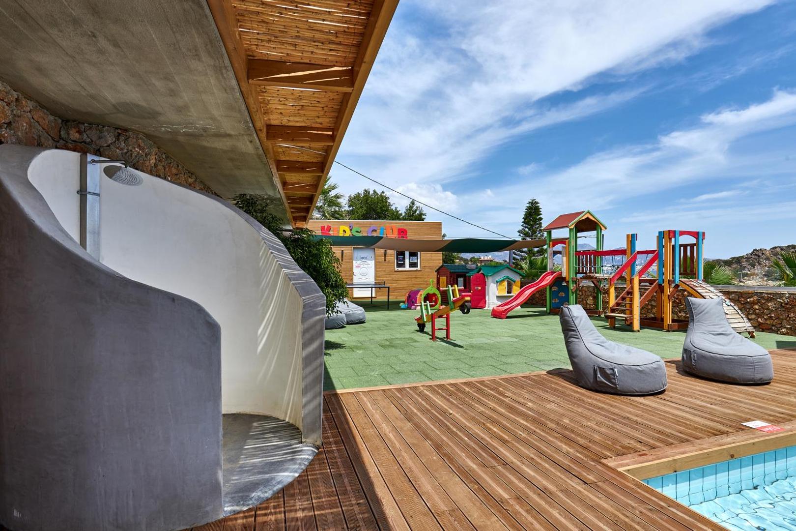 Blue Marine Resort & Spa bērnu klubs ar rotaļu laukumu, slidkalniņiem un sēžammaisiem pie āra baseina saulainā dienā.