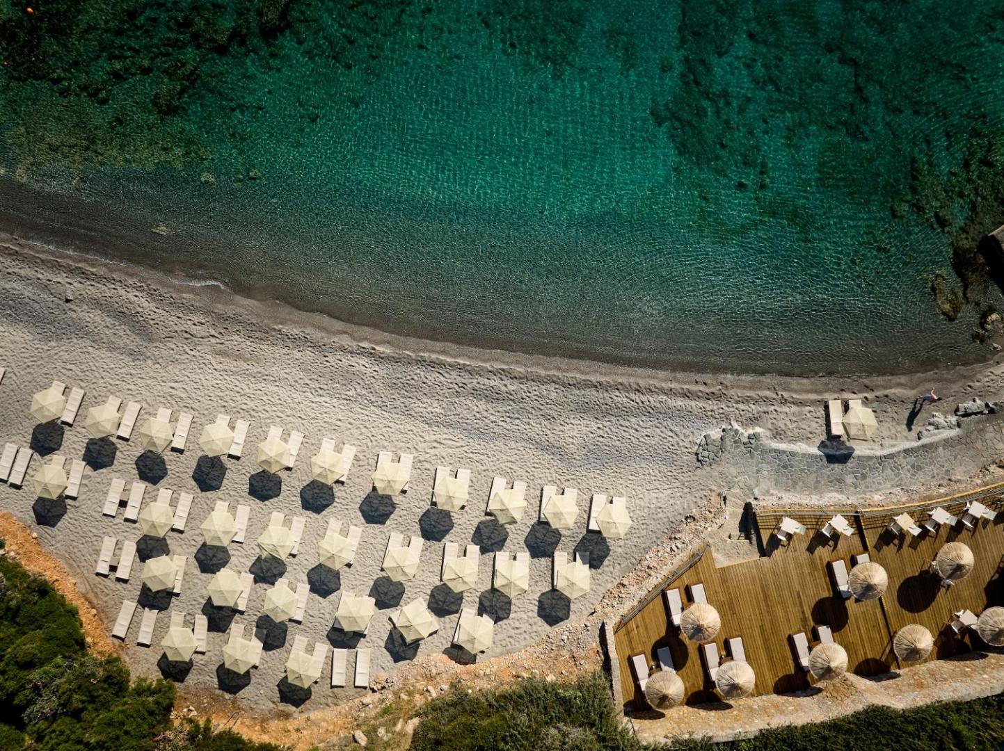 Blue Marine Resort & Spa privātā pludmale no putna lidojuma — saulessargi un sauļošanās krēsli pie dzidra tirkīza ūdens Krētā