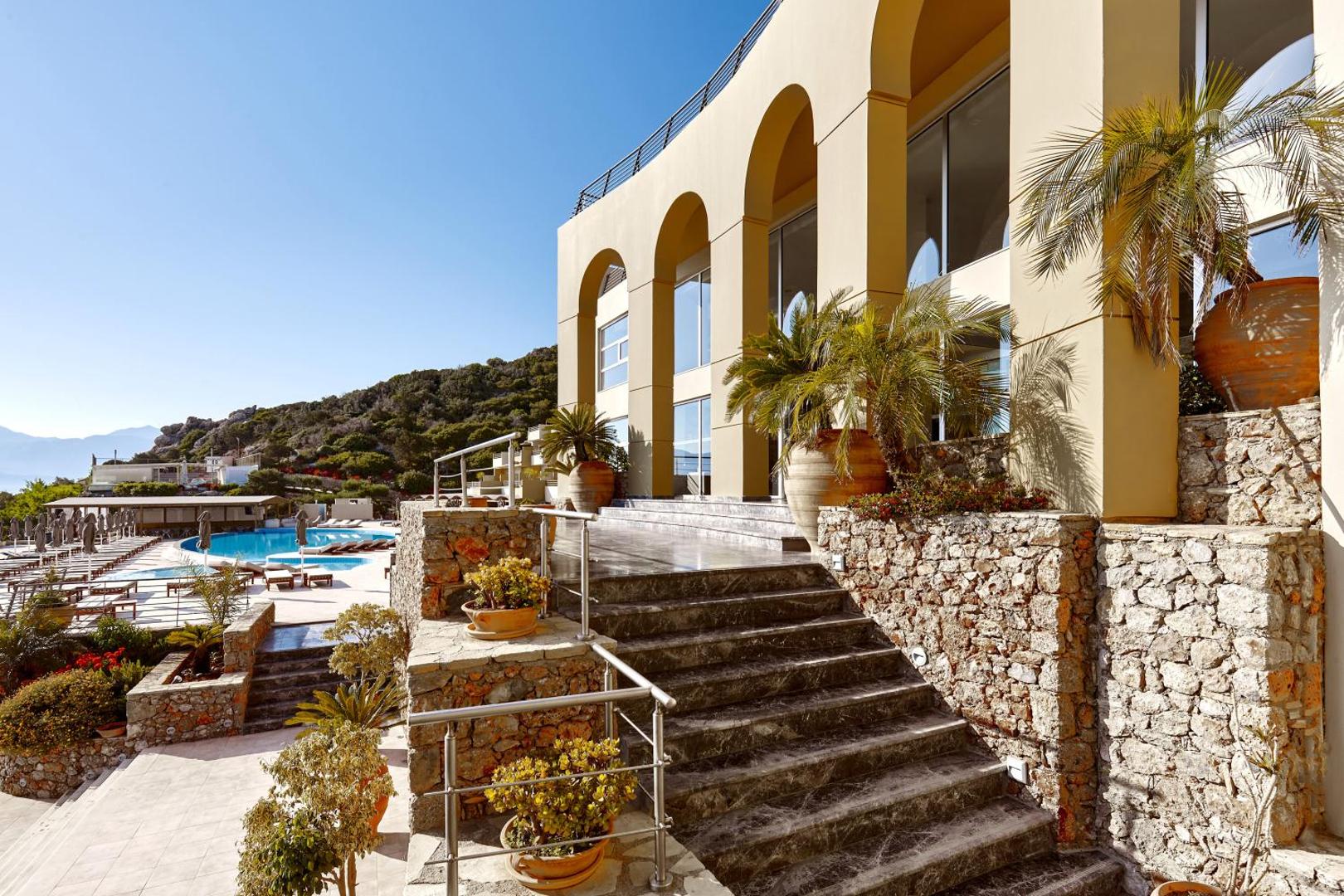 Blue Marine Resort & Spa galvenā ieeja ar akmens mūra kāpnēm, arkām un skatu uz āra baseinu saulainā dienā