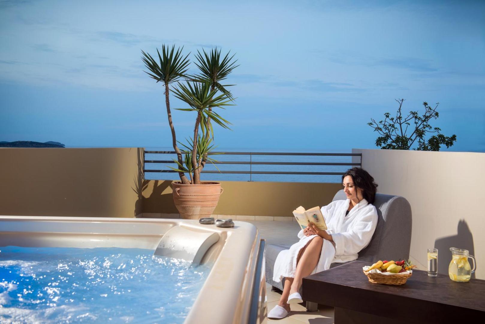 Sieviete baltā halātā lasa grāmatu pie džakuzi uz Blue Marine Resort & Spa terases ar skatu uz jūru