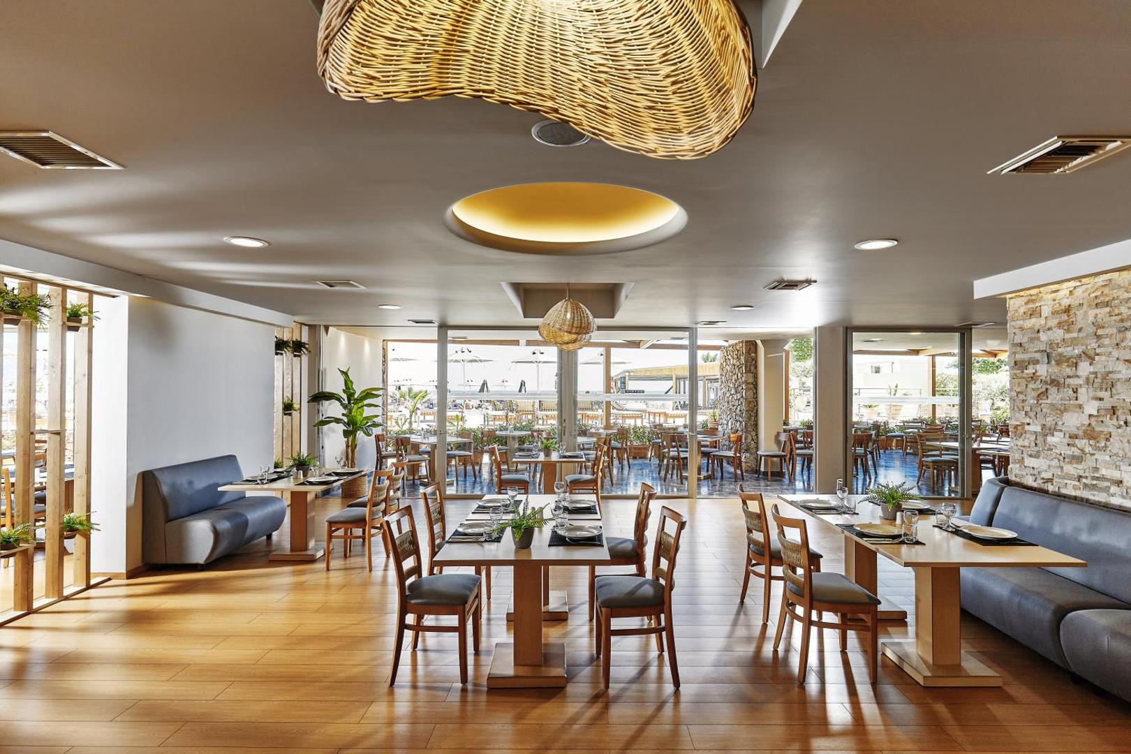Gaiša Blue Marine Resort & Spa restorāna zāle ar koka galdiem, moderniem krēsliem un lieliem logiem uz āra terasi