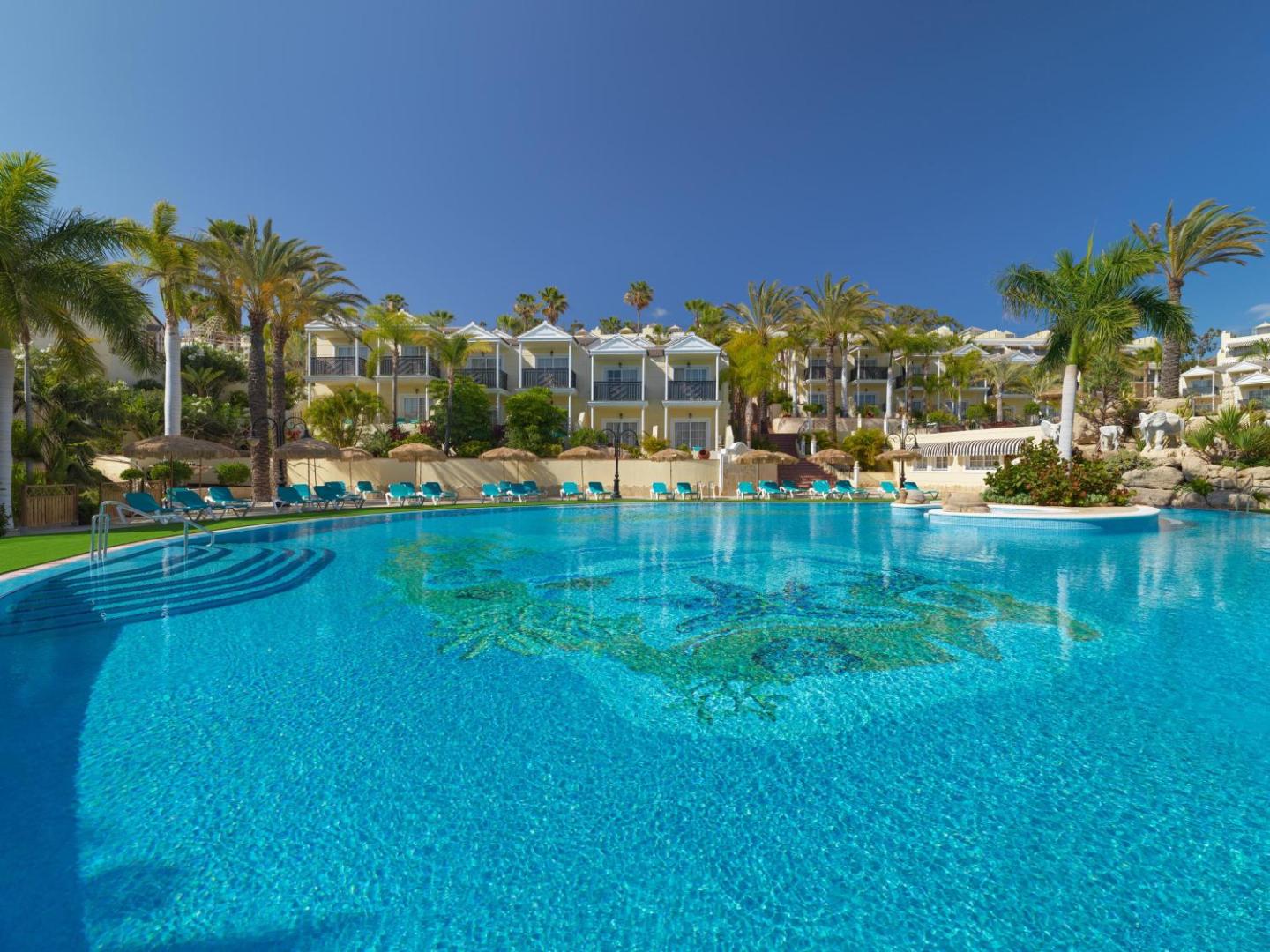 Gran Oasis Resort lielais āra baseins ar zilu ūdeni, palmām un viesnīcas korpusiem fonā saulainā dienā Tenerifē