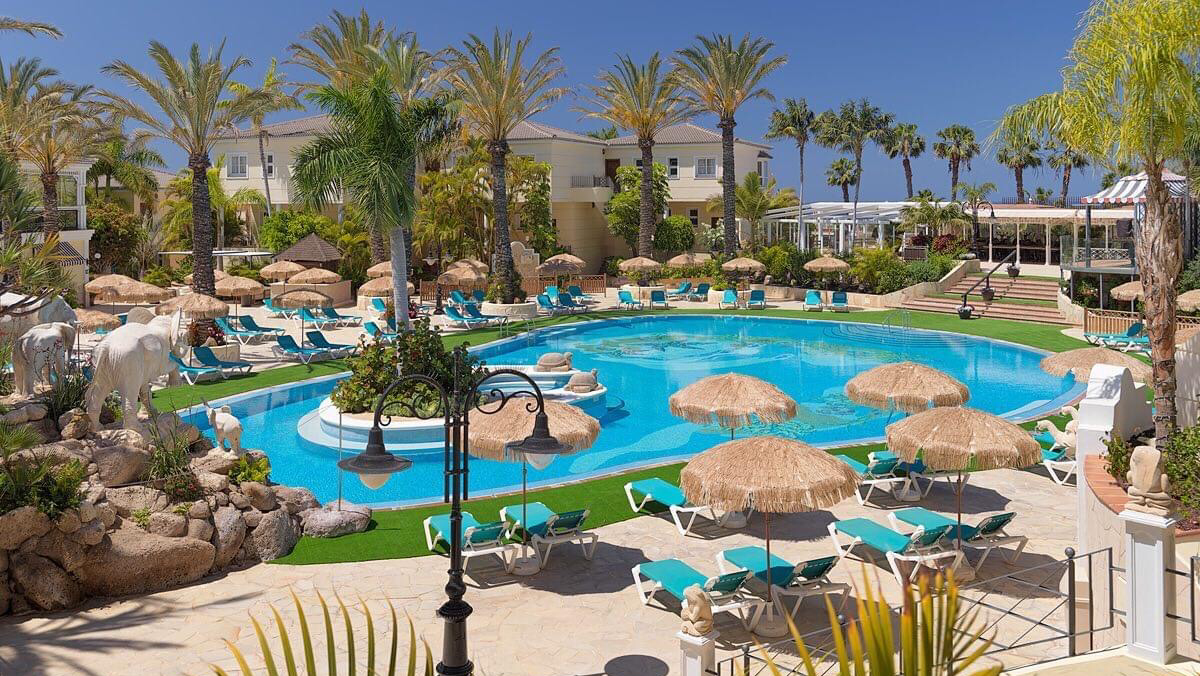 Gran Oasis Resort galvenais baseins ar salmu saulessargiem un ziloņu dekorācijām Tenerifē — plaša sauļošanās zona un viesnīcas korpusi fonā
