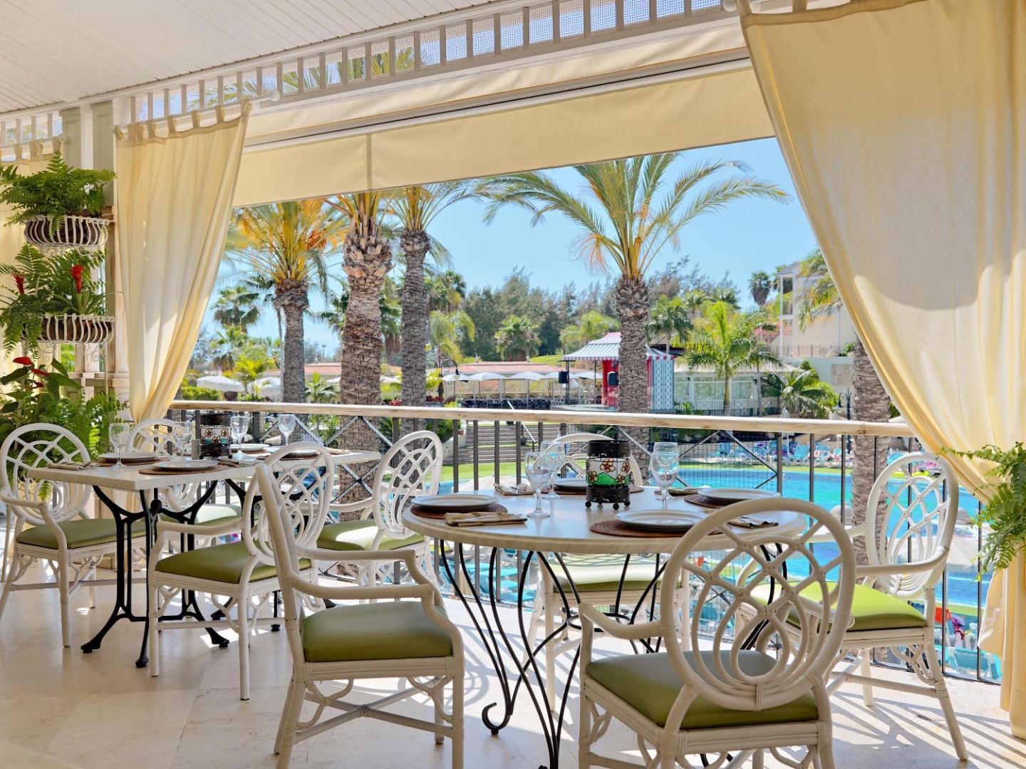Gran Oasis Resort restorāna terase ar balti klātiem galdiem un skatu uz palmu dārzu un baseinu Tenerifē