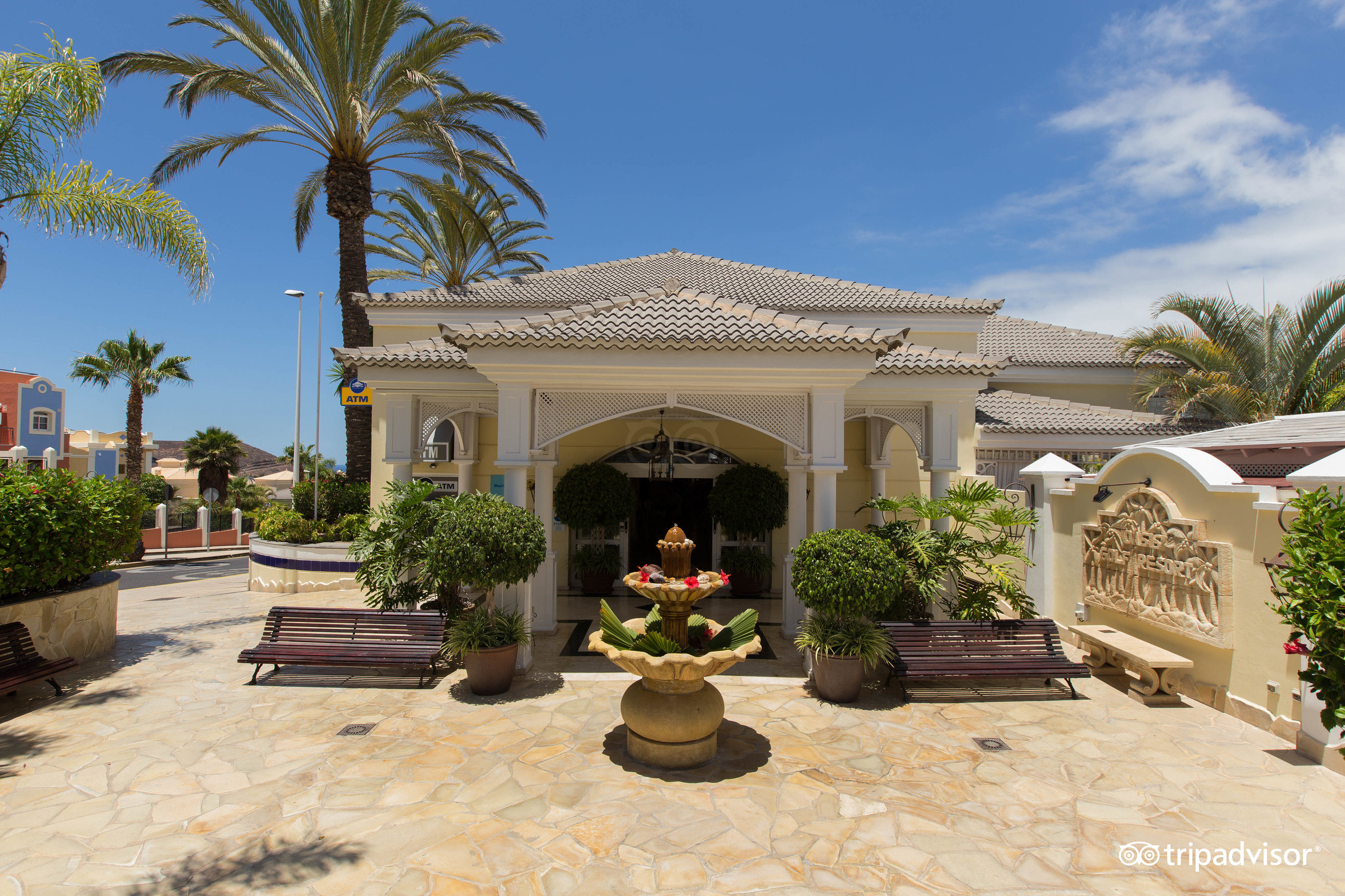 Gran Oasis Resort ieeja ar dekoratīvu strūklaku, soliņiem un palmu pie ieejas mezgla Tenerifē