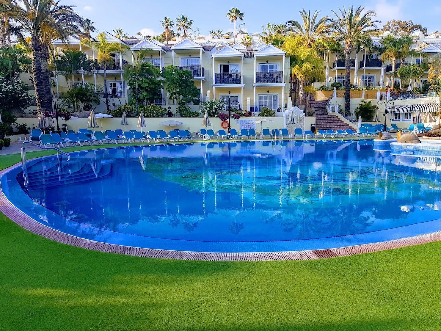 Gran Oasis Resort numuru korpusi pie liela, zila baseina Tenerifē — gaišas ēkas ar balkoniem un koptu zaļo zonu