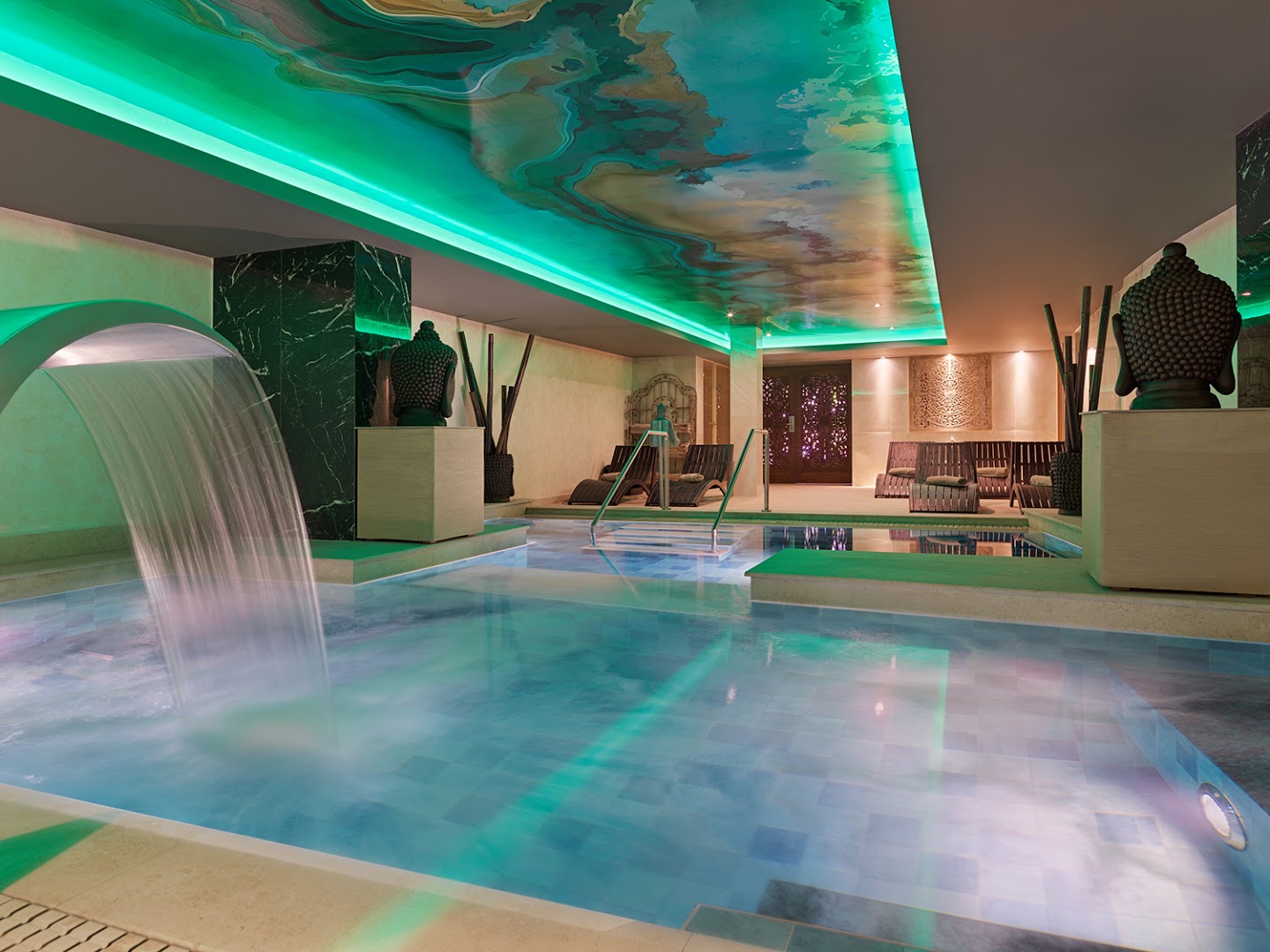 Gran Oasis Resort iekštelpu baseins ar kaskādes ūdenskritumu un atpūtas krēsliem spa zonā Tenerifē mierpilnai vakara relaksācijai