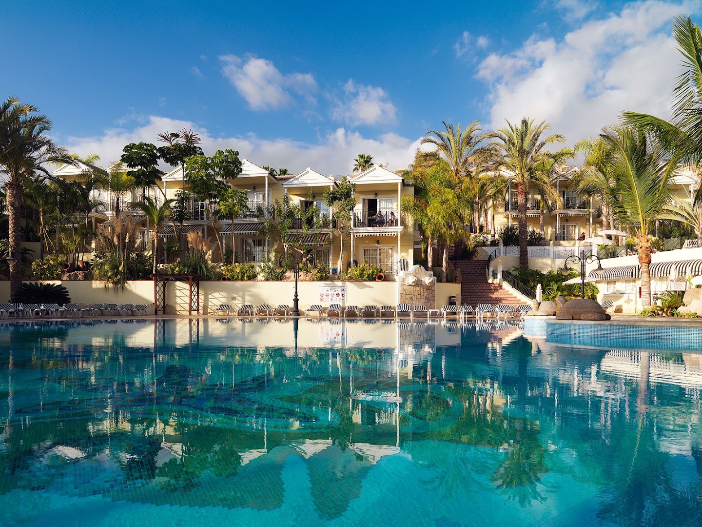 Gran Oasis Resort galvenais baseins ar zilu mozaīku un viesnīcas korpusiem fonā zem skaidrām debesīm Tenerifē