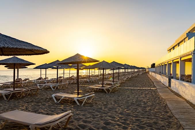 Civitel Creta Beach privātā smilšu pludmale ar daudziem saulessargiem un sauļošanās krēsliem saulrieta gaismā Krētā