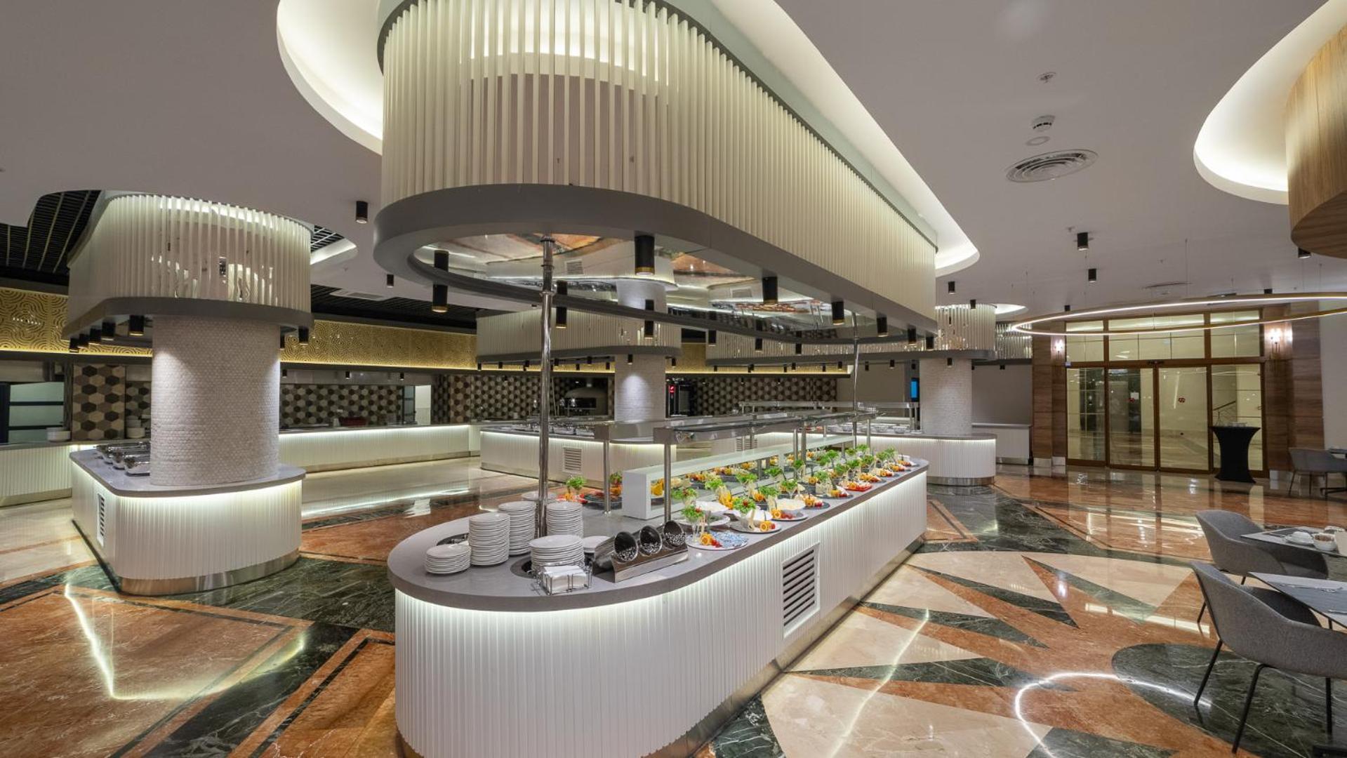 Numa Club Side bufetes zona ar uzkodām un salātiem uz modernām servēšanas līnijām gaišā restorāna telpā