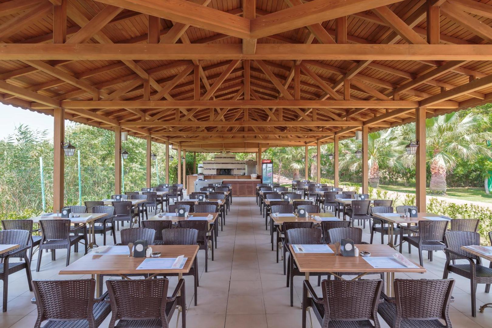 Sunis Elita Beach Resort brīvdabas restorāns zem koka nojumes ar pītiem krēsliem un skatu uz dārzu Sides reģionā, Turcijā