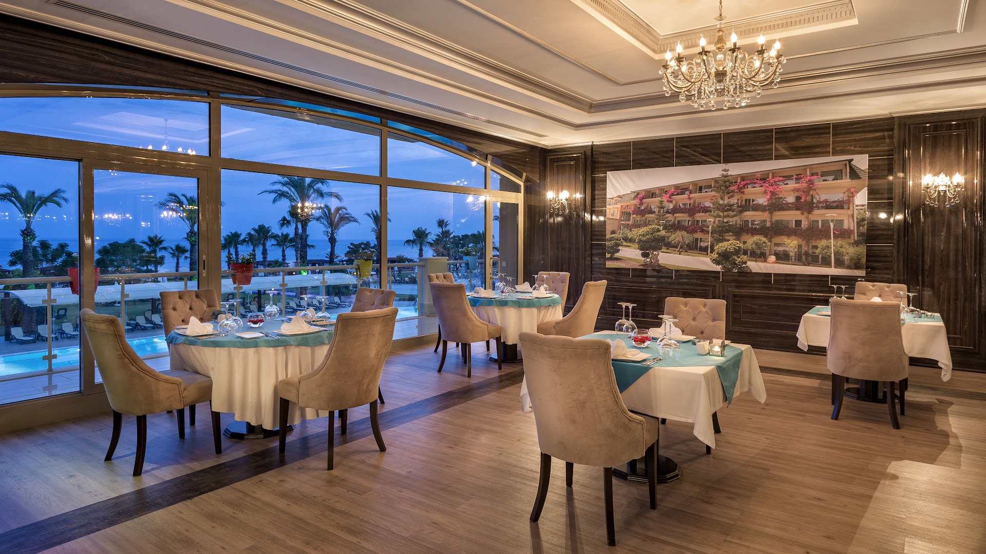 Pine Beach Belek a la carte restorāns ar skatu uz jūru saulrietā, eleganti klāti galdi un grezna lustra