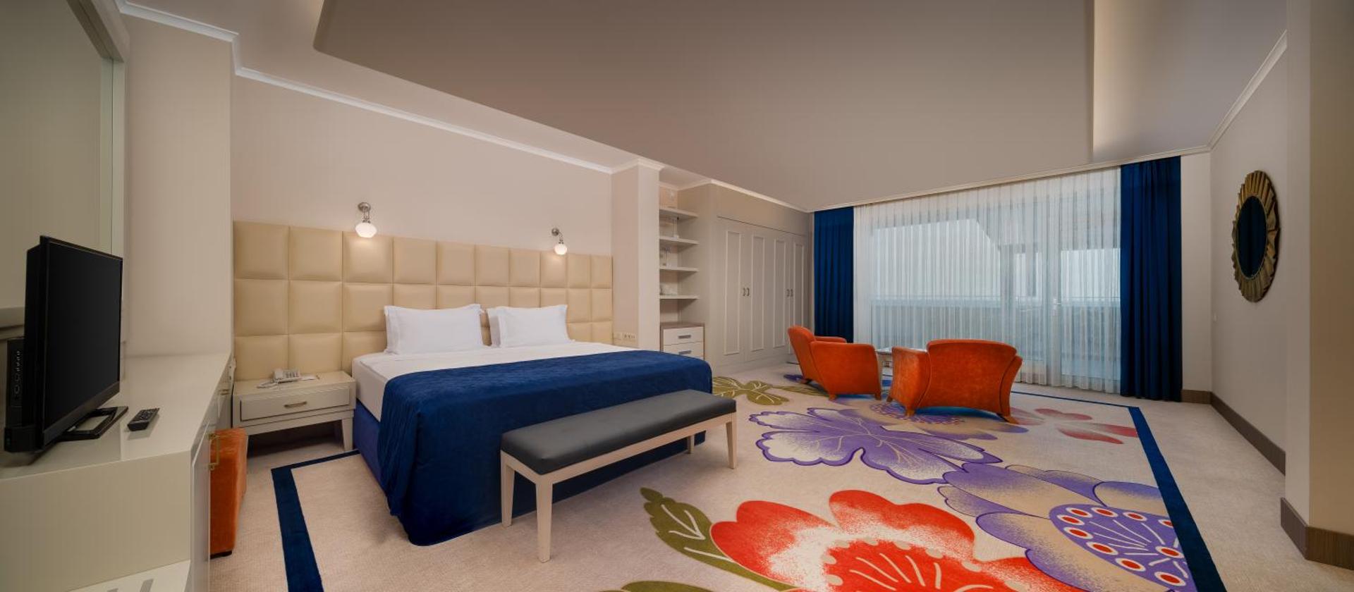 Pine Beach Belek plašs guļamistabas numurs ar lielu gultu, ziliem akcentiem un krāsainu paklāju ar ziedu rakstiem