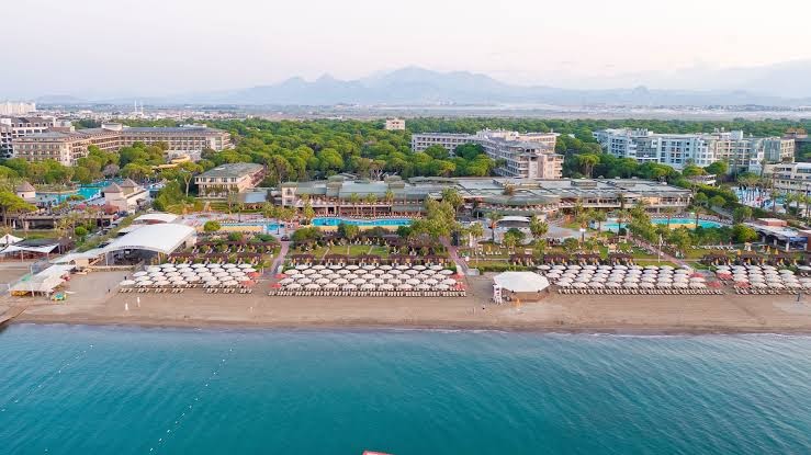 Pine Beach Belek viesnīcas panorāmas skats no putna lidojuma Belekā, Turcijā — plaša teritorija ar baseiniem, smilšu pludmali un apkārtējiem priežu mežiem