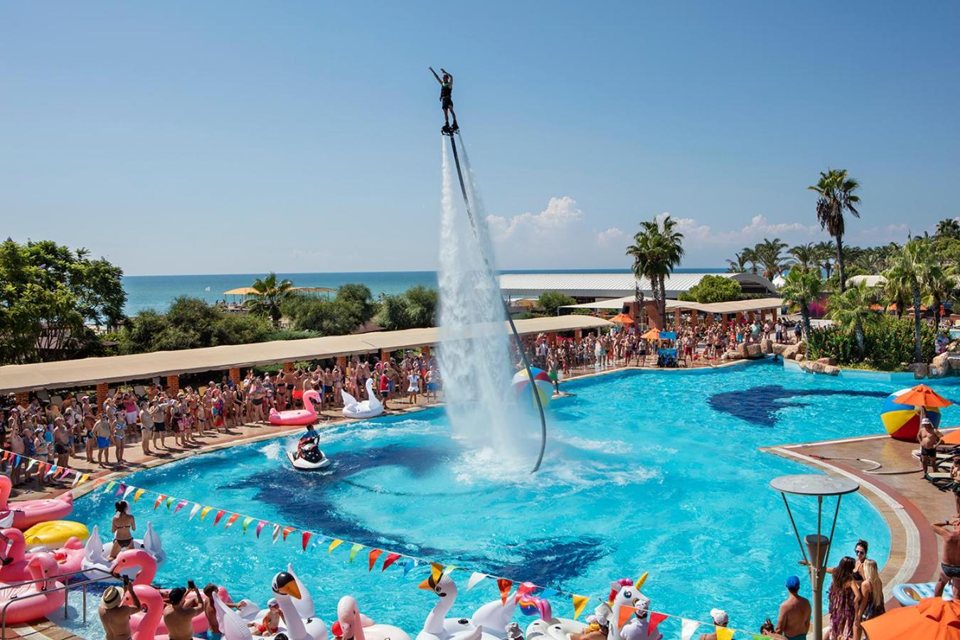Pine Beach Belek āra baseins ar flyboard šovu, apkārt sauļošanās krēsli, palmas un piepūšamās rotaļlietas Belekas piekrastē