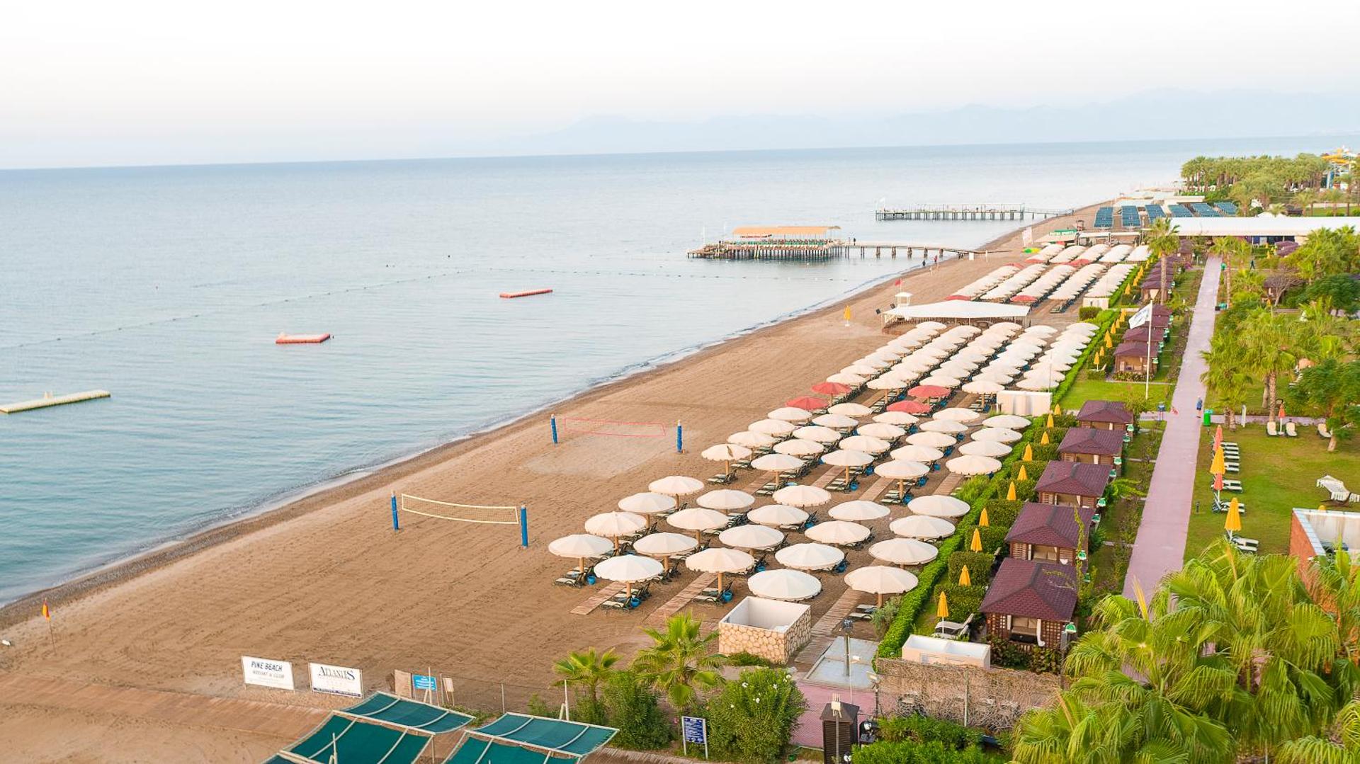 Pine Beach Belek privātā smilšu pludmale ar saulessargiem, sauļošanās krēsliem, volejbola laukumu un koka piestātni jūrā