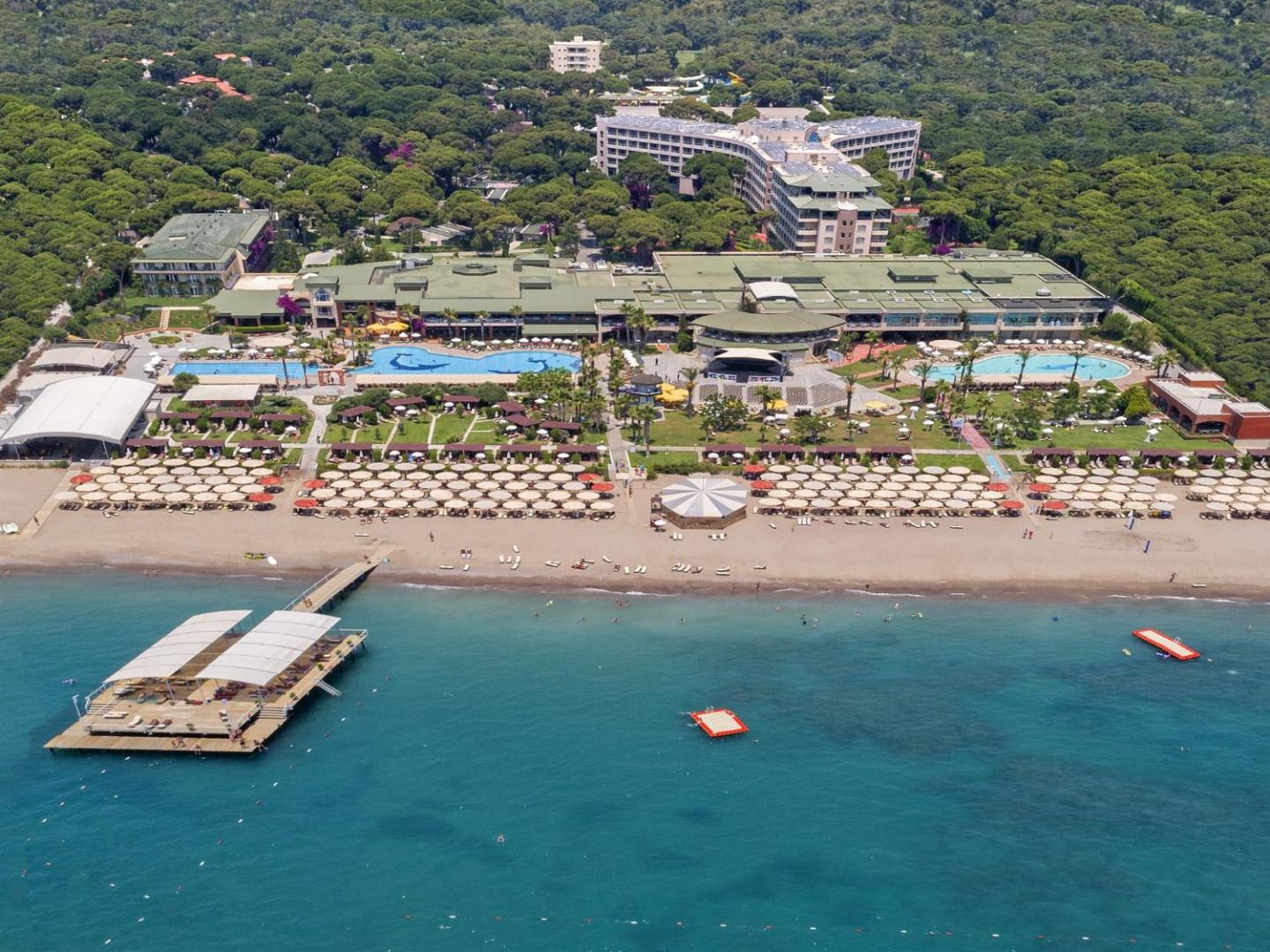 Pine Beach Belek viesnīcas galvenā ēka un dārza teritorija no putna lidojuma, ko ieskauj blīvs priežu mežs Belekas kūrortā.