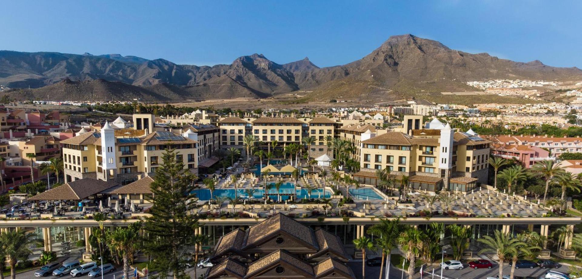 GF Gran Costa Adeje panorāmas skats uz viesnīcas kompleksu Tenerifē ar āra baseiniem, sauļošanās terasēm un iespaidīgu kalnu fonu