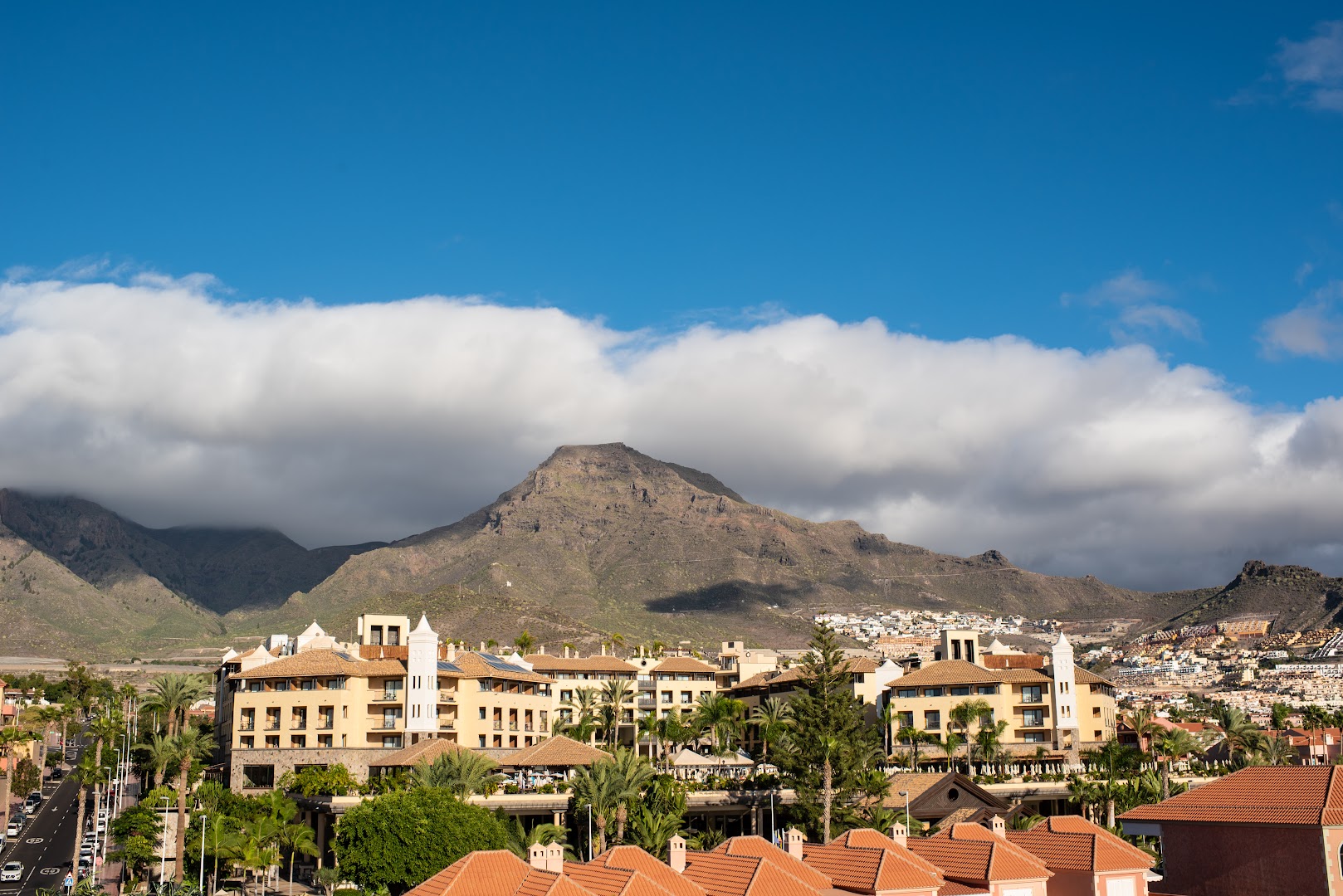 GF Gran Costa Adeje viesnīcas ēkas arhitektūra un apkārtne Tenerifē ar skatu uz kalniem un zilu debesu fonu