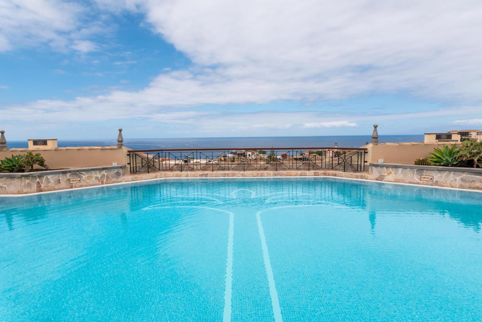 Skats no GF Gran Costa Adeje baseina ar pārplūdes malu uz okeāna horizontu un piekrastes ainavu Tenerifē.