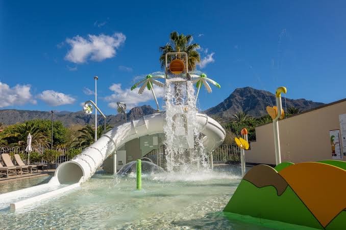 GF Gran Costa Adeje bērnu baseins ar ūdens slidkalniņu un atrakcijām Tenerifē uz kalnu un palmu fona