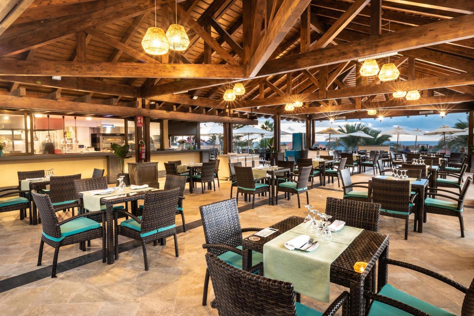 GF Gran Costa Adeje mājīgs ēdienkartes restorāns ar koka sijām, pītiem krēsliem un siltu apgaismojumu vakara stundā.