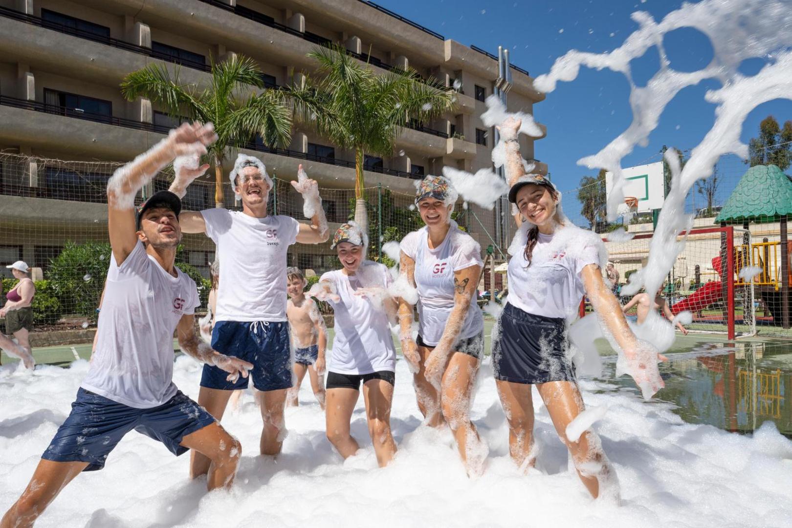 Animācijas komanda un viesi izbauda putu ballīti GF Fañabe viesnīcas āra aktivitāšu zonā Tenerifē saulainā dienā