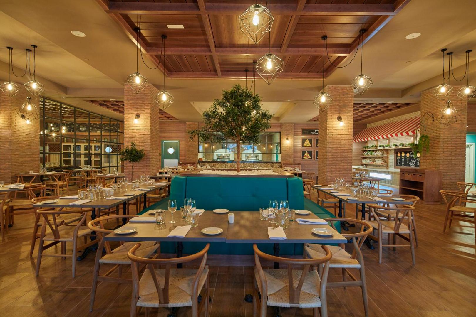 Bahia Principe Fantasia Tenerife itāļu restorāna interjers ar koka apdari, dekoratīvu koku centrā un siltu apgaismojumu