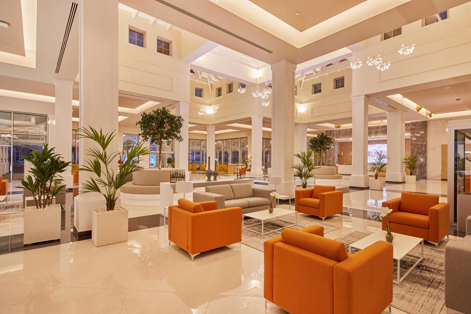 Bahia Principe Fantasia Tenerife plašais un gaišais lobby bārs ar oranžiem atpūtas krēsliem, augstiem griestiem un dekoratīviem augiem podos