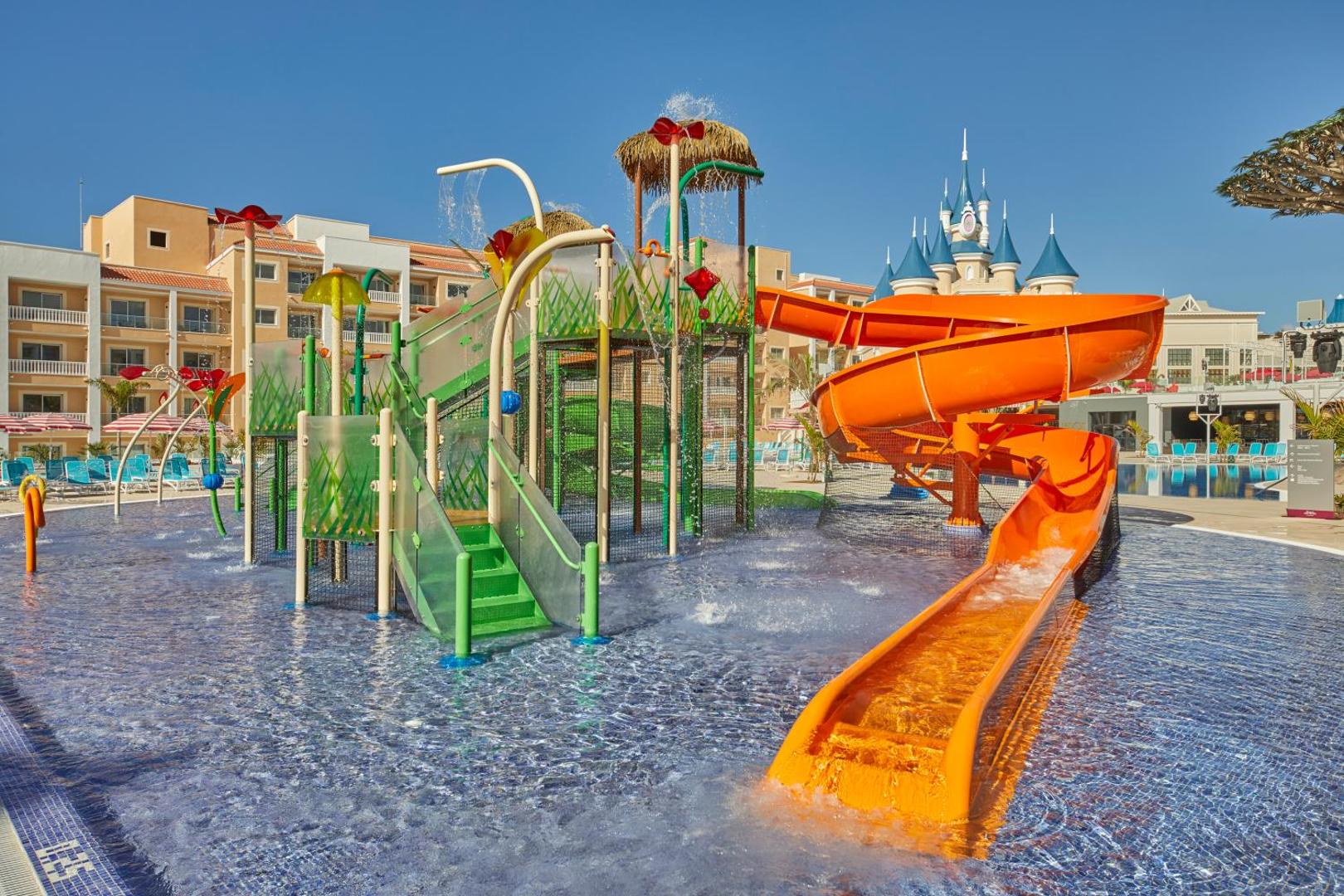 Bahia Principe Fantasia Tenerife bērnu ūdens atrakciju parks ar slidkalniņiem, seklu baseinu un pasaku pili fonā Tenerifē.