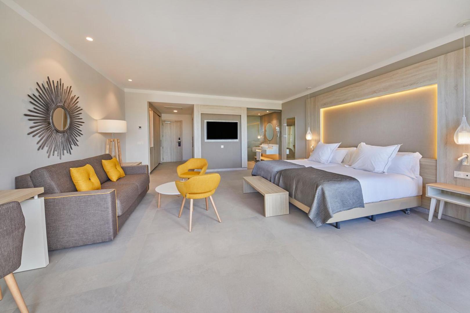 Bahia Principe Fantasia Tenerife moderns numurs ar lielu gultu, dīvānu, dzelteniem krēsliem un atvērtu vannasistabas zonu