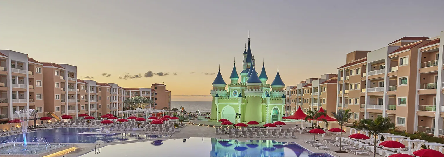 Bahia Principe Fantasia Tenerife viesnīcas panorāmas skats ar centrālo pili, lielu baseinu un atpūtas zonu saulrietā Tenerifes piekrastē.