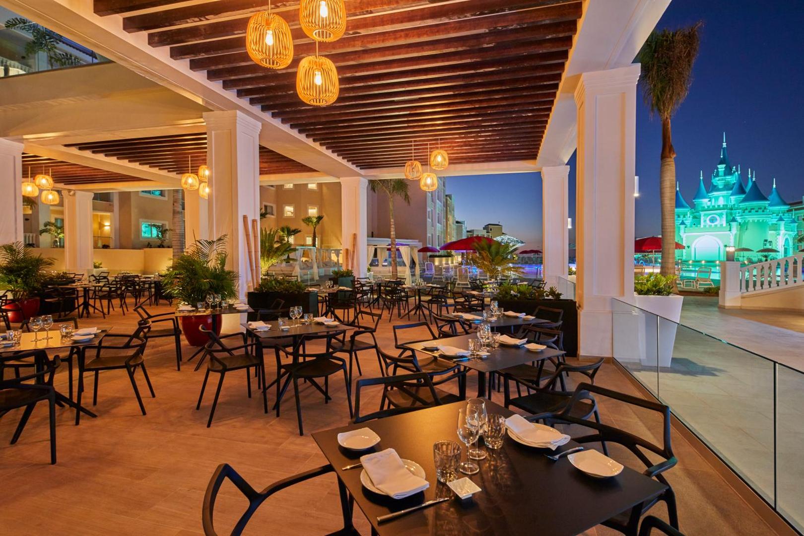 Viesnīcas Bahia Principe Fantasia Tenerife āra terases restorāns vakarā ar skatu uz izgaismoto pili un baseina zonu