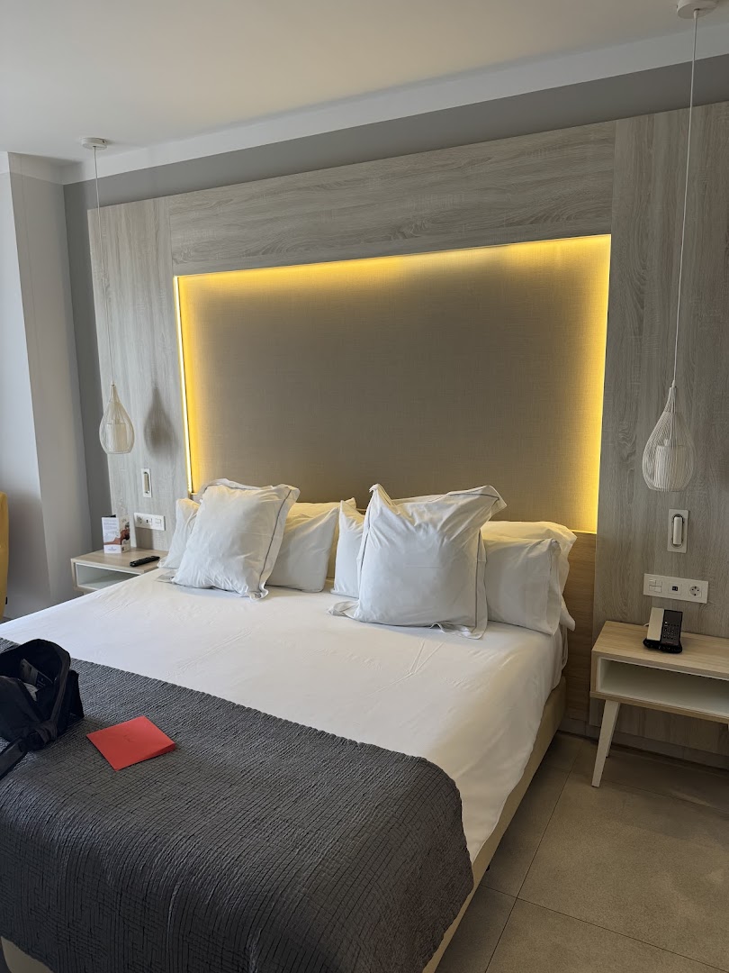 Bahia Principe Fantasia Tenerife viesnīcas numurs ar lielu gultu, gaišu koka apdari un siltu dekoratīvo apgaismojumu virs galvgaļa.