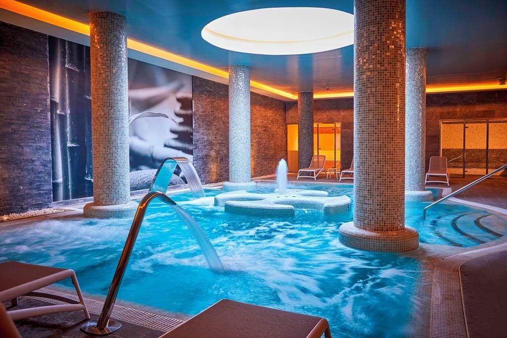 Bahia Principe Fantasia Tenerife viesnīcas iekštelpu spa baseins ar masāžas strūklām, mozaīkas kolonnām un relaksācijas zonu Tenerifē, Spānijā.