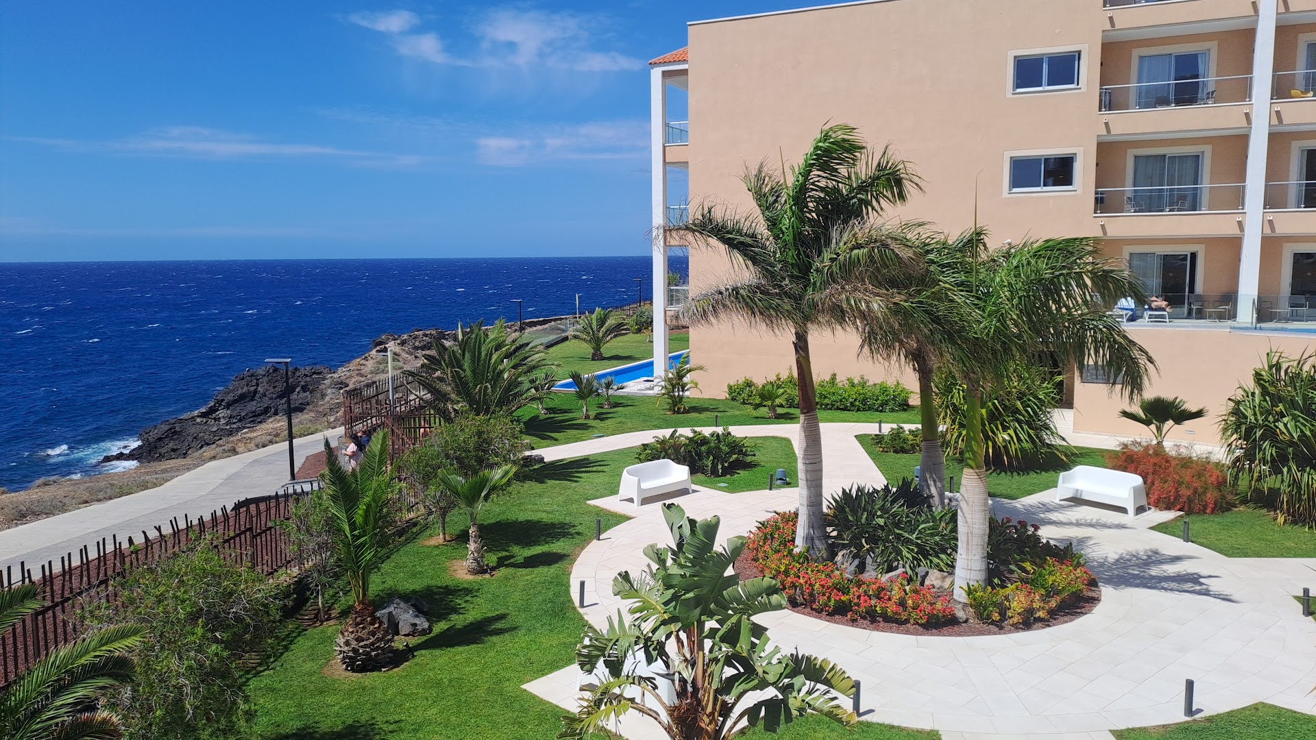 Bahia Principe Fantasia Tenerife skats no augšas uz dārzu ar palmām, atpūtas soliem un zilo okeānu piekrastē