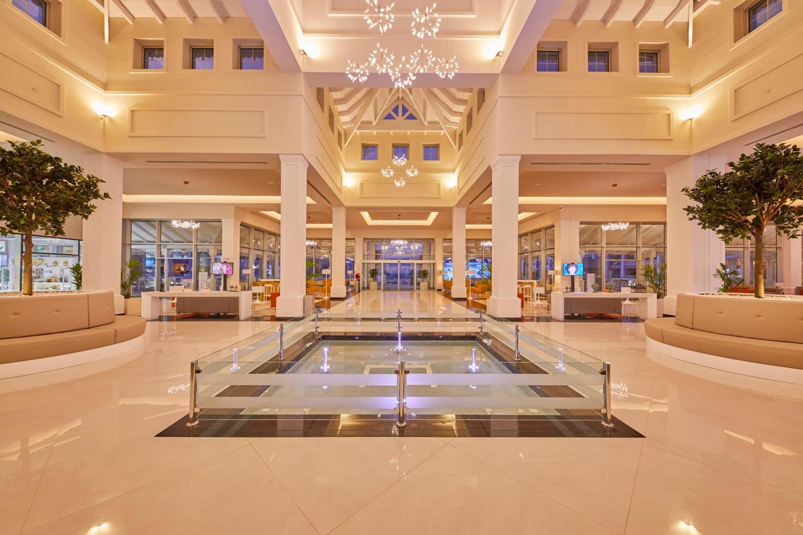Bahia Principe Fantasia Tenerife viesnīcas vestibils ar dekoratīvu baseinu centrā un greznām lustrām — skats uz ieeju un atpūtas zonām