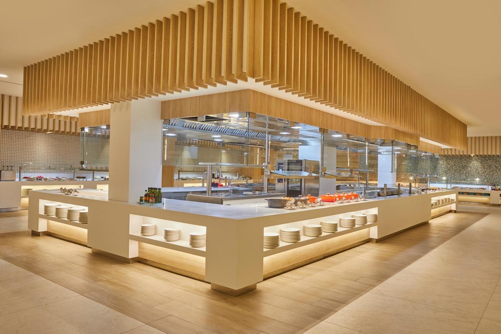 Bahia Principe Fantasia Tenerife galvenā restorāna bufetes zona ar plašu ēdienu izvēli — moderns interjers ar koka elementiem un atvērto virtuvi