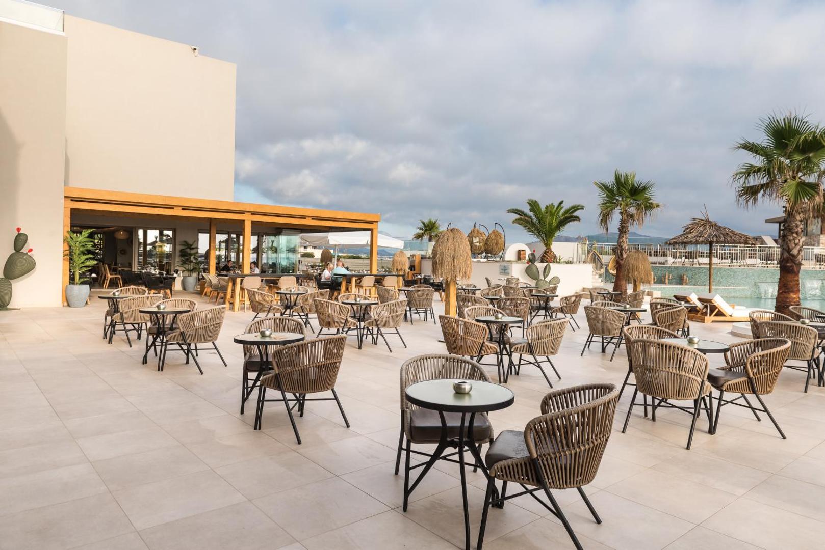 Pepper Sea Club plašā āra atpūtas terase ar pītiem krēsliem, nelieliem galdiņiem un palmām pie baseina malas