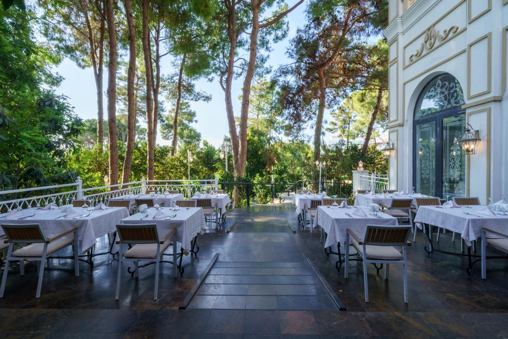 Ali Bey Resort Sorgun restorāna āra terase ar klātiem galdiem priežu meža ielenkumā Sidē, Turcijā — eleganta vide maltītēm svaigā gaisā