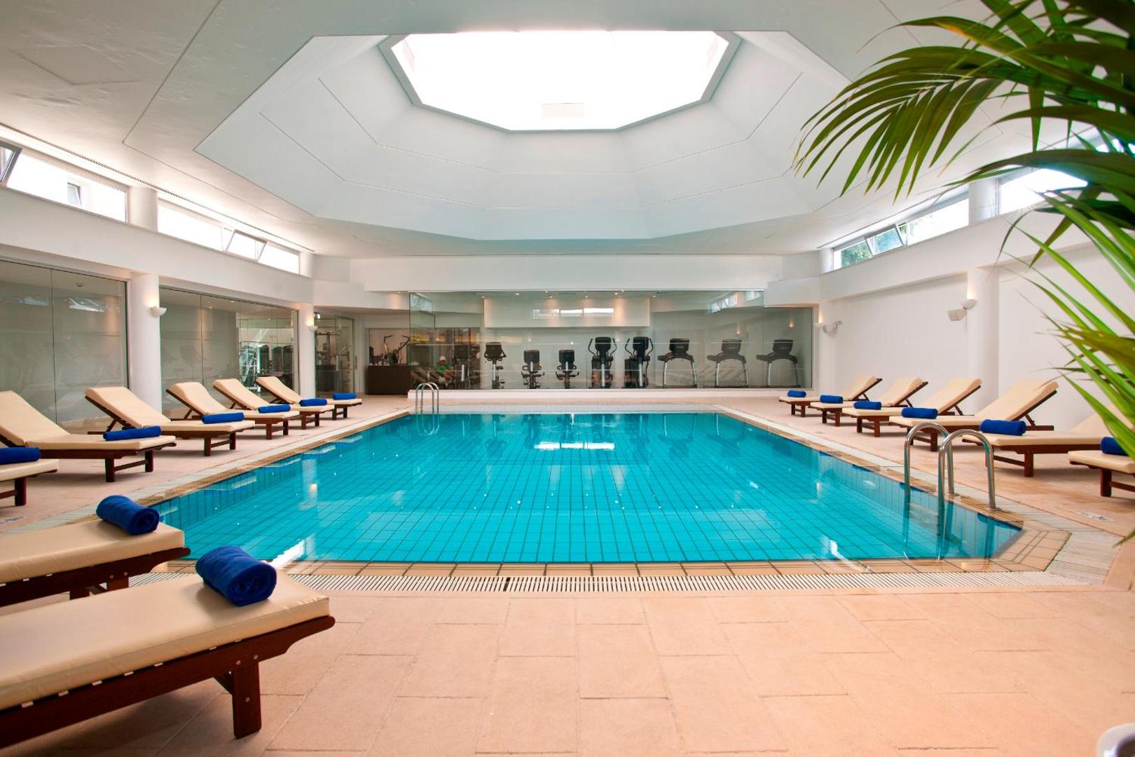 The Royal Apollonia iekštelpu baseins ar apsildi un atpūtas krēsliem — gaiša spa zona ar dabisko apgaismojumu no griestu loga