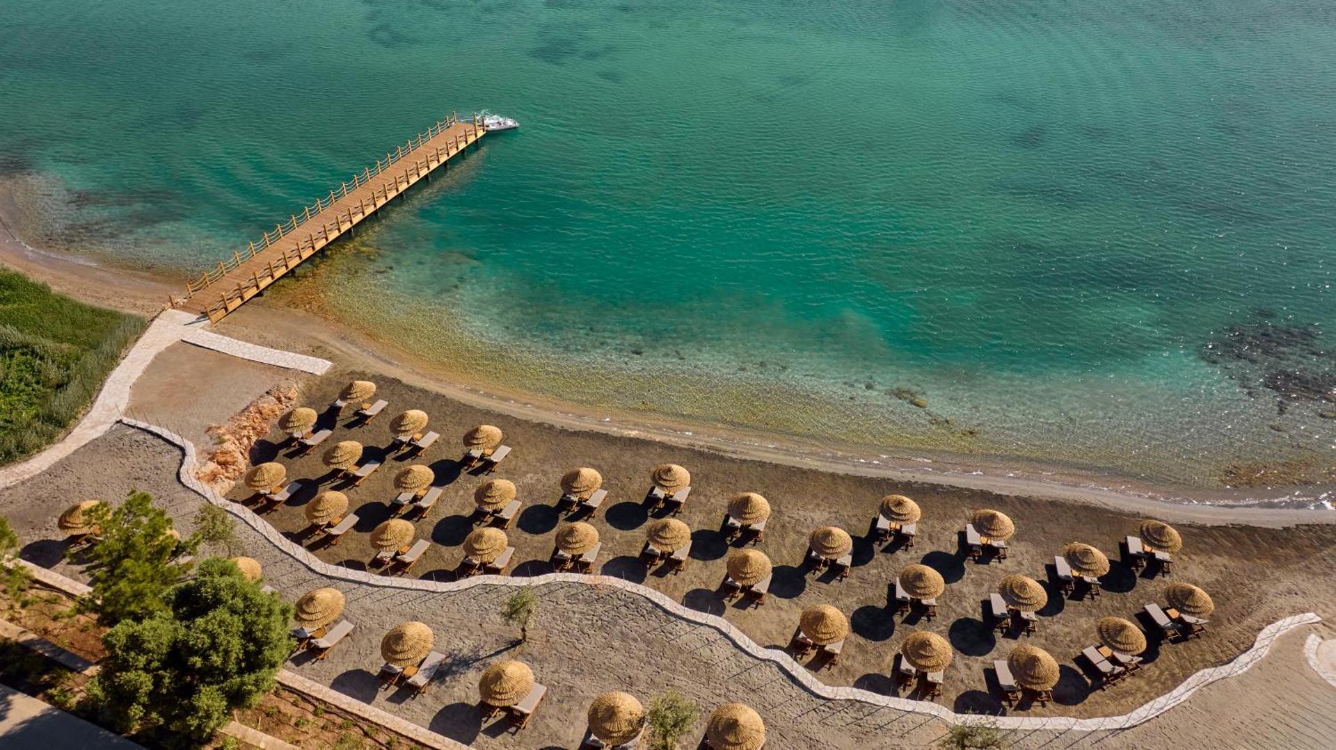 Anda Barut Collection skats no putna lidojuma uz pludmali ar salmu saulessargiem un garu koka laipu tirkīza ūdenī